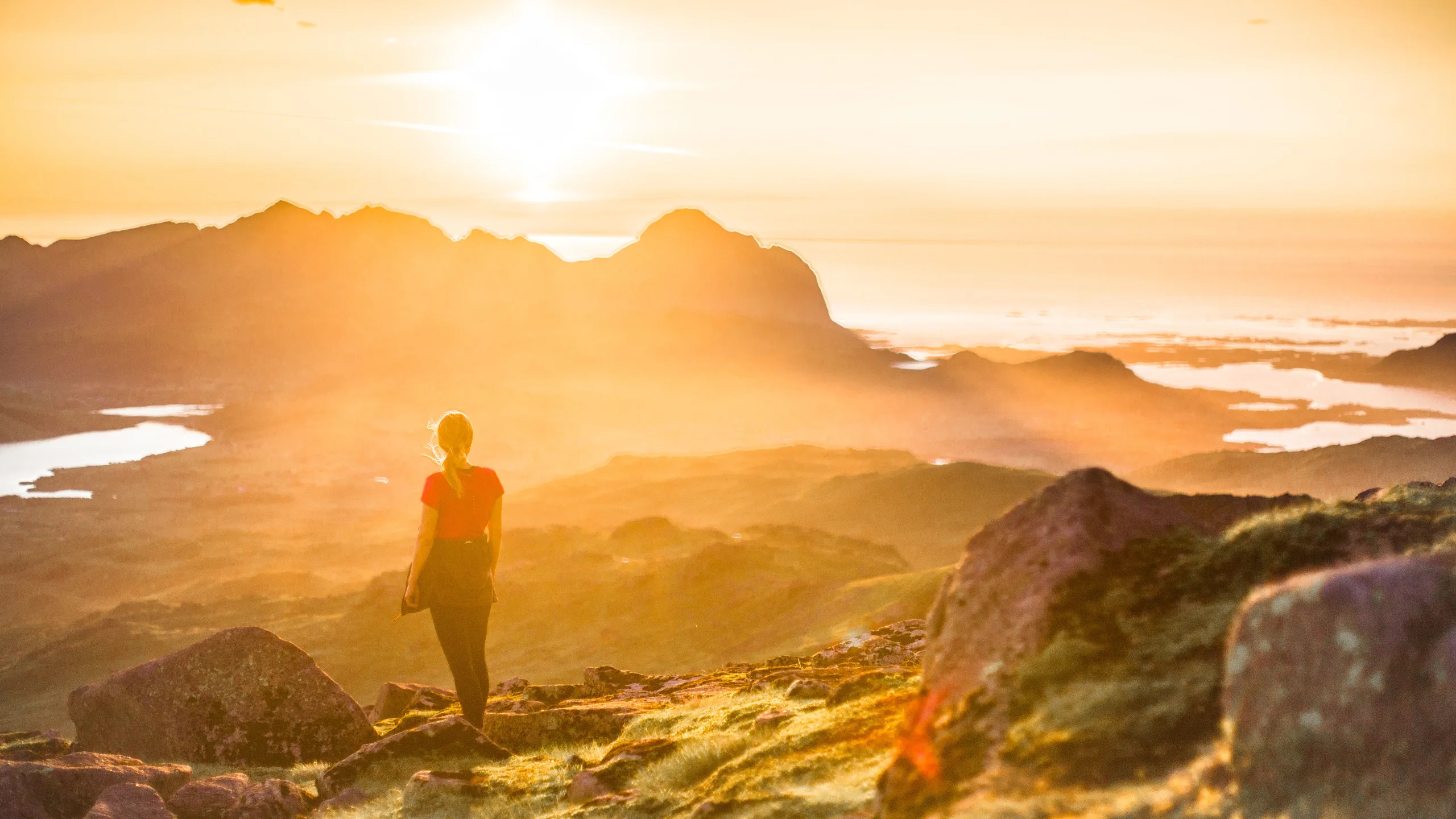 Woman looking at the sunset from a mountain top in Lofoten